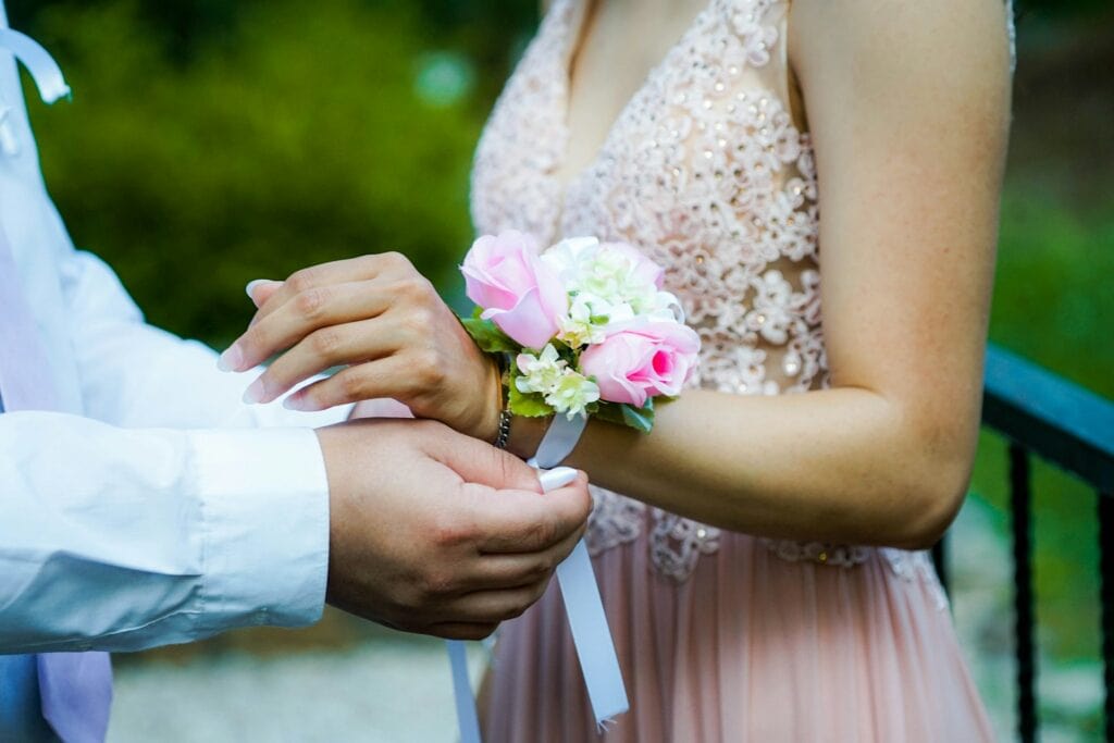 un jeune homme place une boutonnière au poignet de son date pour un bal de promo