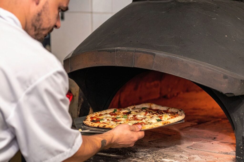 personne mettant au four une pizza lors d'un atelier culinaire d'evg