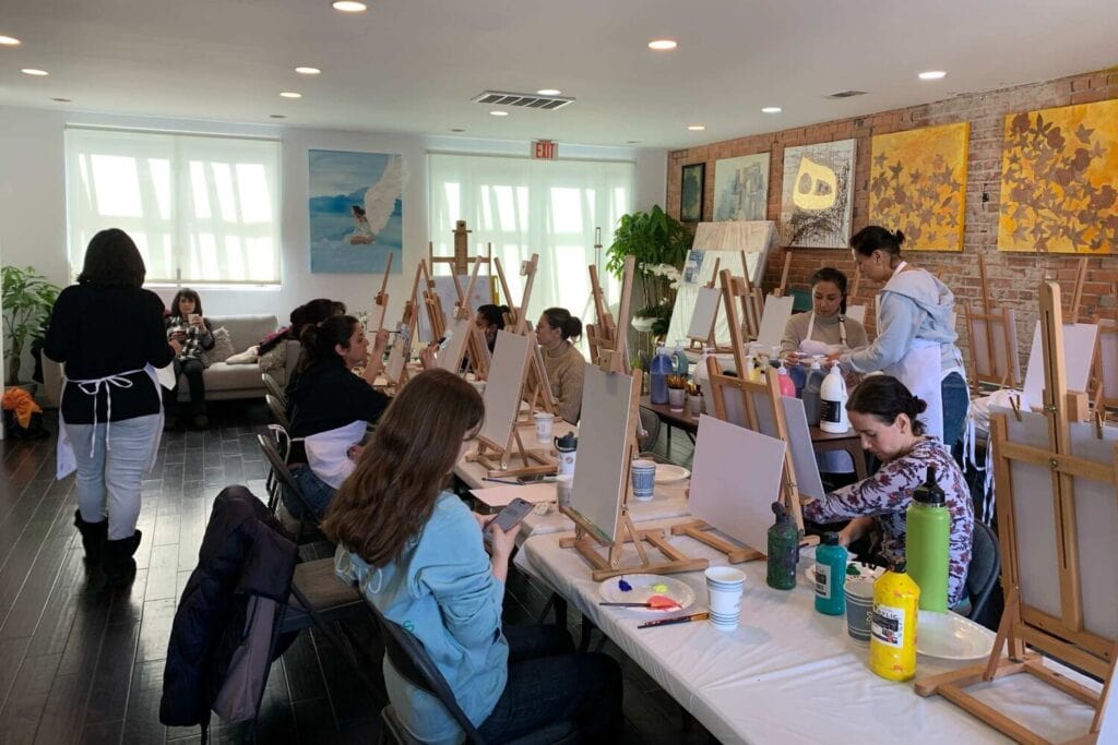 Groupe d'adultes installé devant des chevalets pour un atelier de peinture dans un studio lumineux.