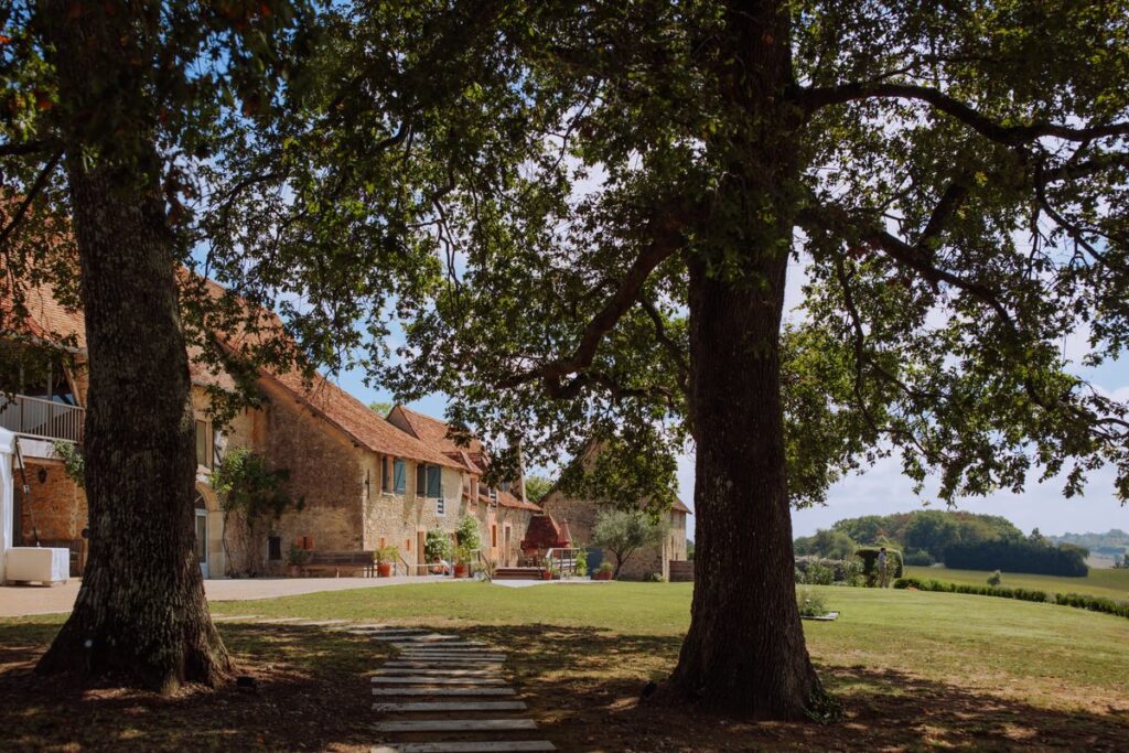Extérieur d'un domaine en pierre avec pelouse arborée et dépendances, idéal pour un événement ou un mariage