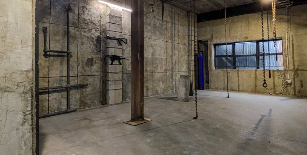 Espace brut d'entrepôt avec murs en béton, chaînes suspendues et atmosphère industrielle marquée
