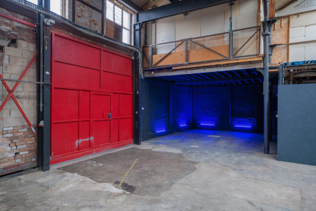 bleue.jpgEntrepôt industriel brut avec grande porte rouge, mur en briques et éclairage bleu LED dans le fond
