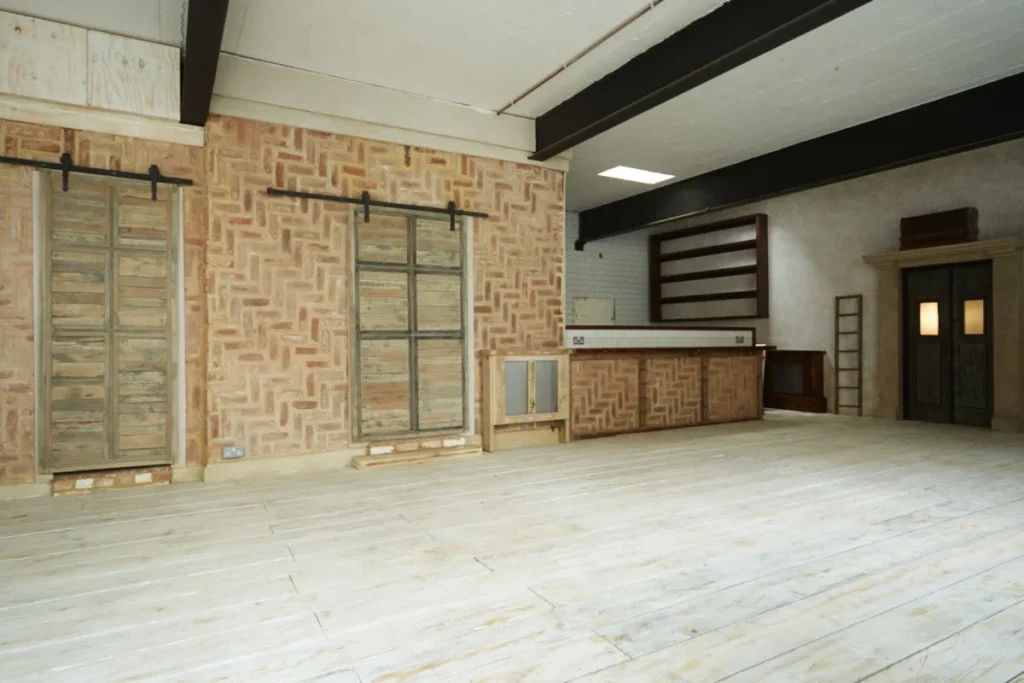 Intérieur d'entrepôt avec mur en briques en chevrons, poutres noires apparentes et parquet bois clair