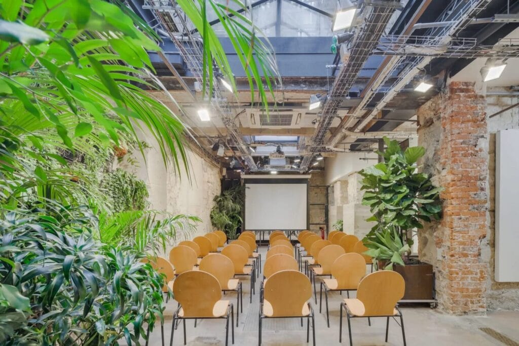 Espace événementiel sous verrière aménagé avec des rangées de chaises et un écran de projection.