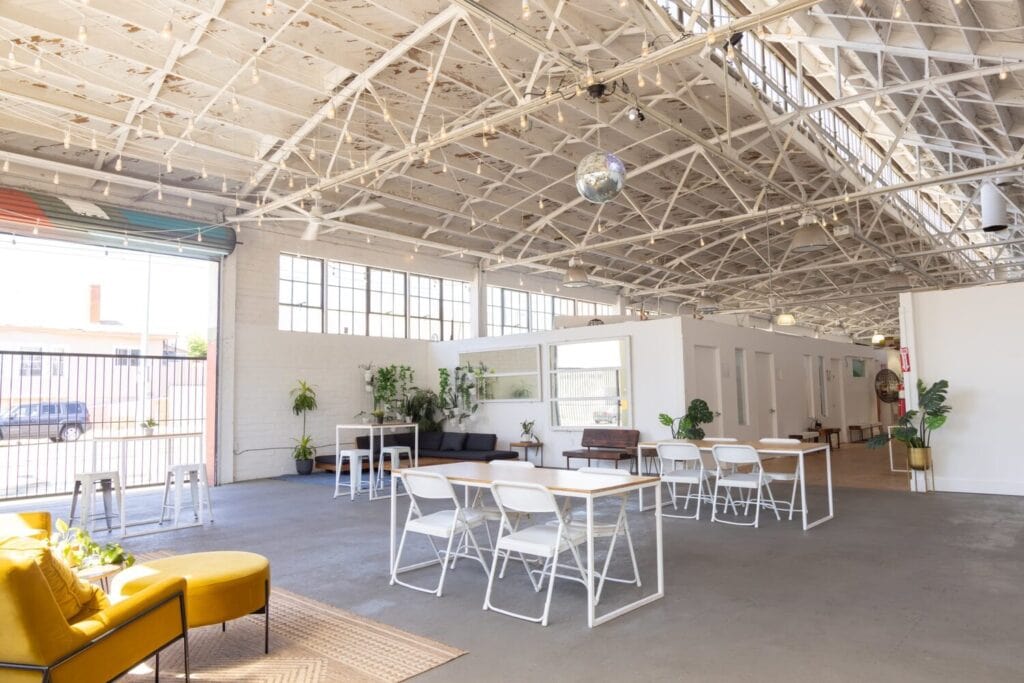 Grand espace industriel lumineux avec verrière, plafond haut, tables et coin salon.