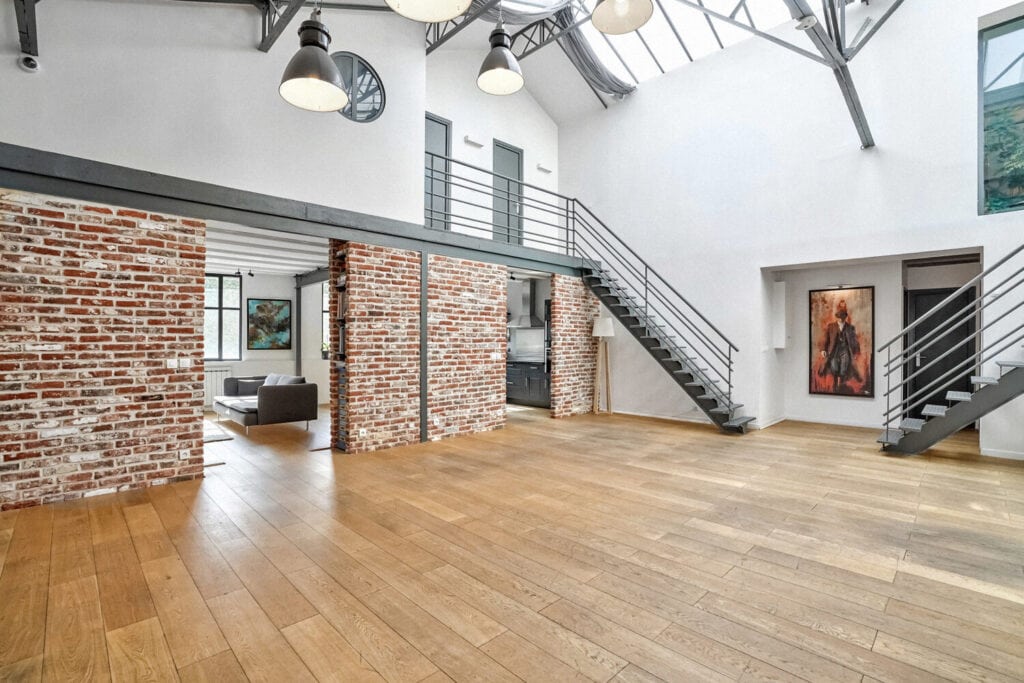 Loft industriel lumineux avec murs en briques, verrière et grand espace central modulable.