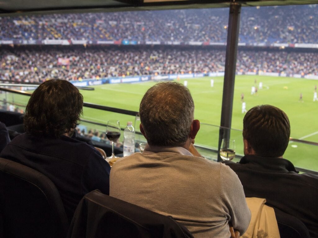 trois hommes regardent le football depuis une loge vip