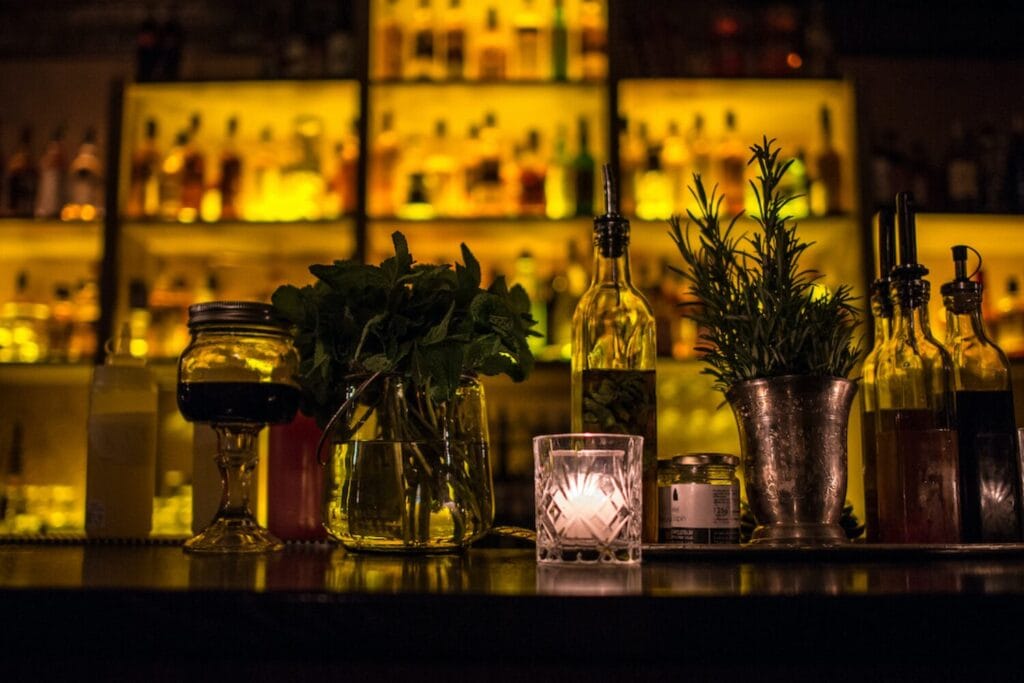 Balise alt	Comptoir du Moonshiner à Paris, éclairé en jaune derrière des plantes et des accessoires de bar