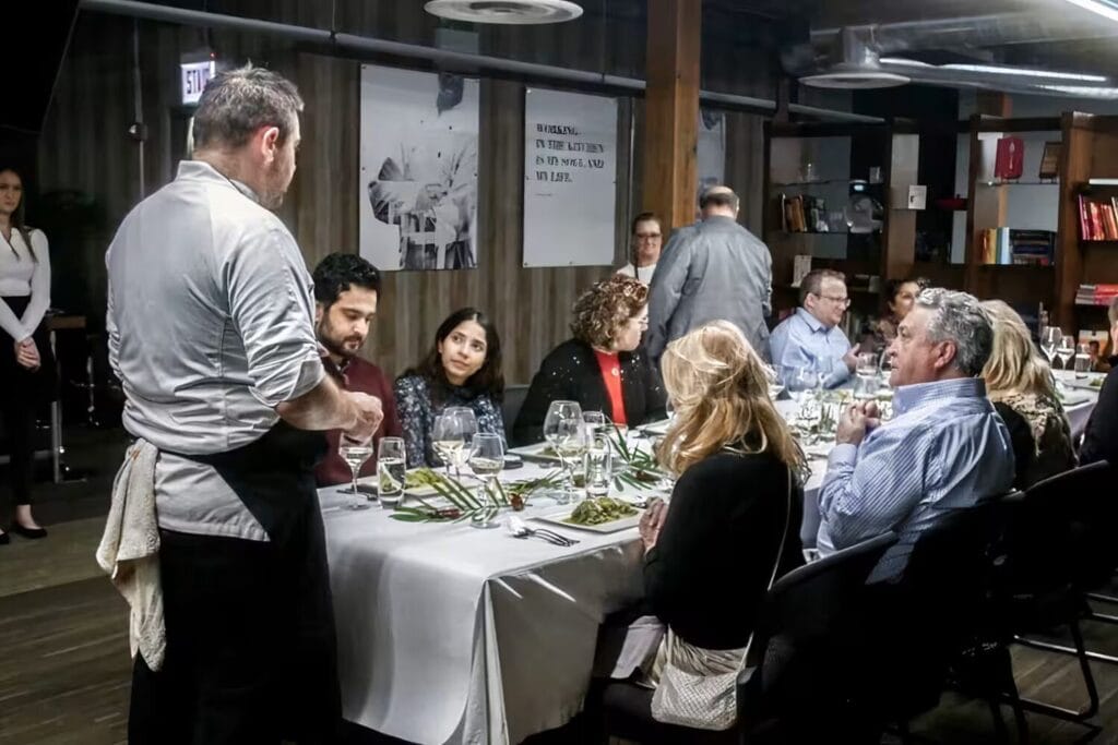 Adultes réunis autour d’une grande table pendant un repas partagé avec service.