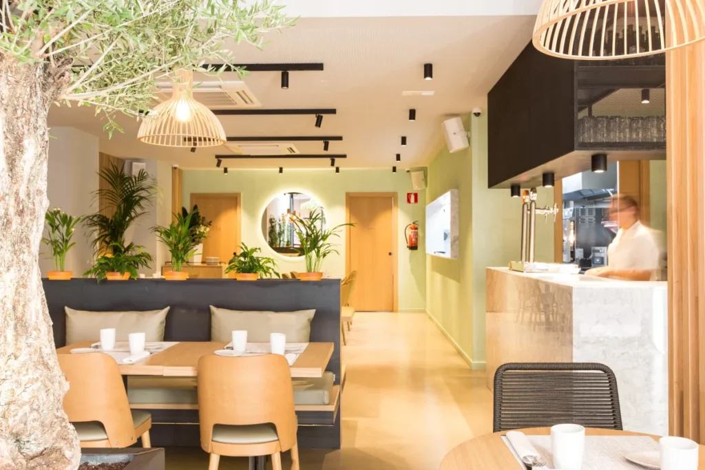 Restaurant contemporain avec décoration végétale, comptoir en marbre et bar visible en fond de salle