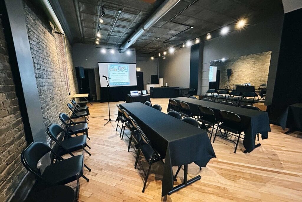 Salle équipée de tables, de chaises et d'un écran de projection pour une présentation.
