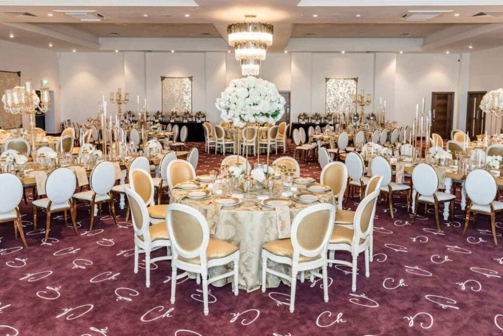 Grande salle de bal aménagée pour un mariage avec tables rondes, fleurs blanches et chandeliers.