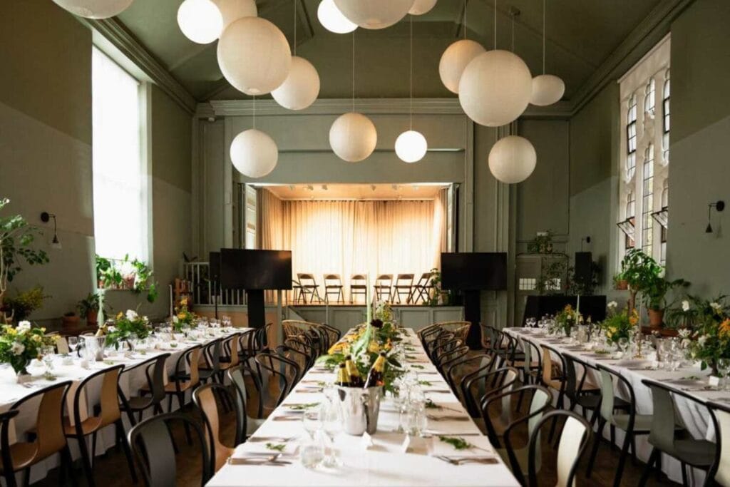 Salle de réception avec scène, longues tables dressées et lanternes en papier suspendues.