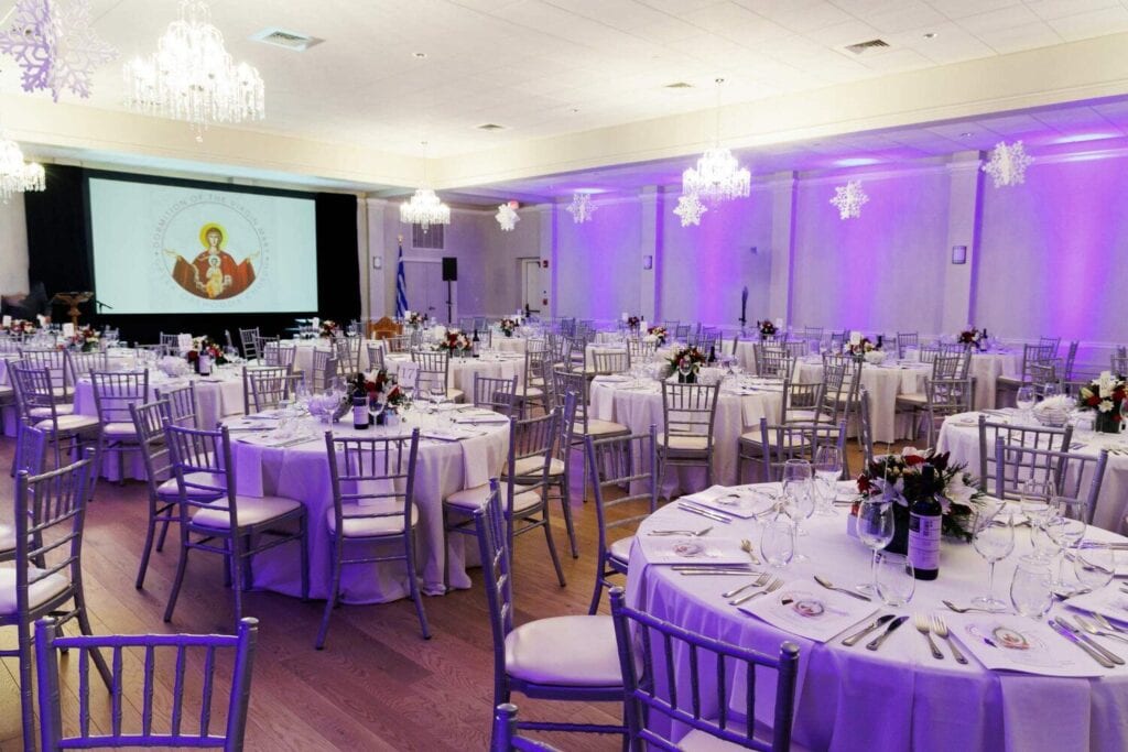 Salle de réception avec tables rondes dressées, chandeliers et éclairage violet.