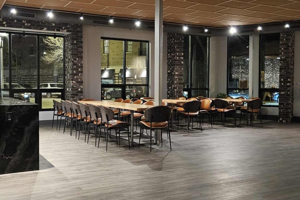 Salle moderne avec une longue table en bois, des chaises et de grandes fenêtres.