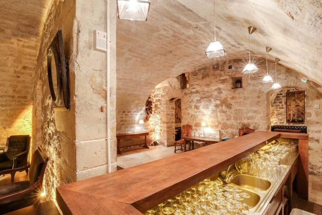 Salle de réception voûtée en pierre avec bar intégré et éclairage chaleureux.