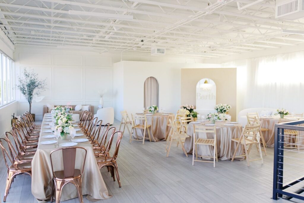 Grande salle lumineuse aux tons poudrés avec tables, chaises et espace libre pour circuler.