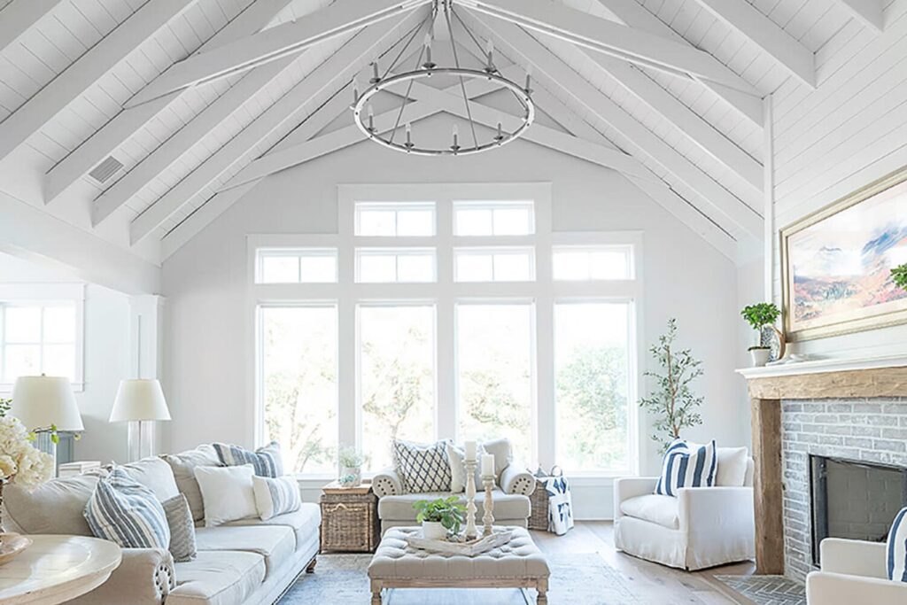 Salon blanc lumineux avec plafond voûté, cheminée, canapé et grandes fenêtres.