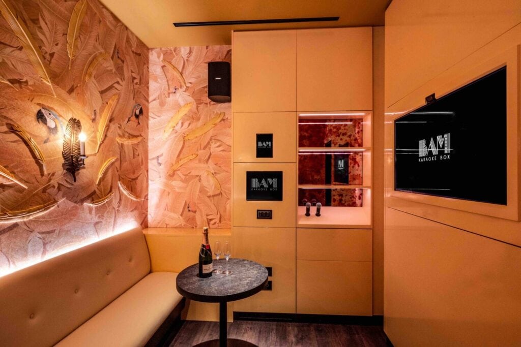 : Salon privé de karaoké avec écran, banquette et table dans une ambiance chaleureuse.