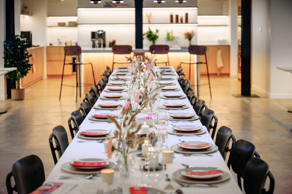 Longue table dressée pour un dîner d'événement privé dans un espace lumineux avec cuisine ouverte en arrière-plan
