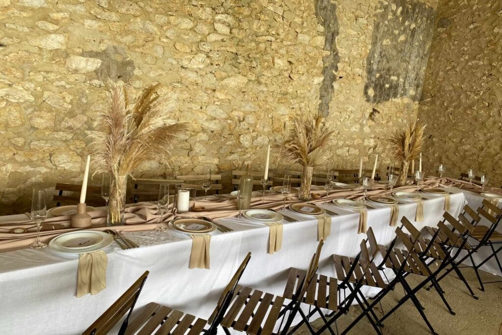 Longue table de réception dressée devant un mur en pierre avec bougies et herbes séchées