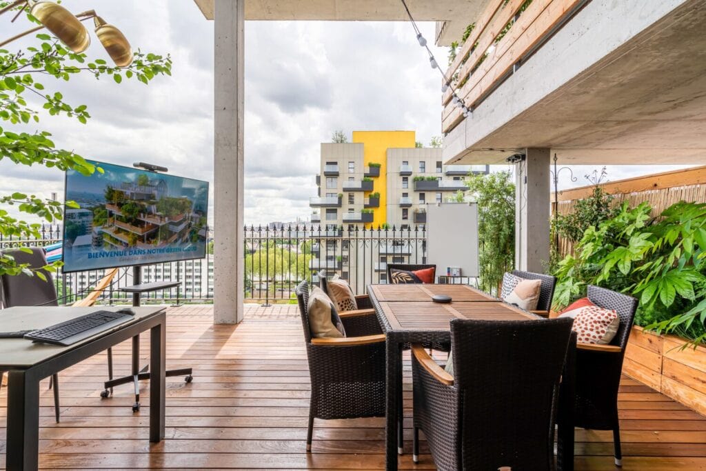 Terrasse de coworking aménagée avec tables, écran, tableau blanc et végétation.