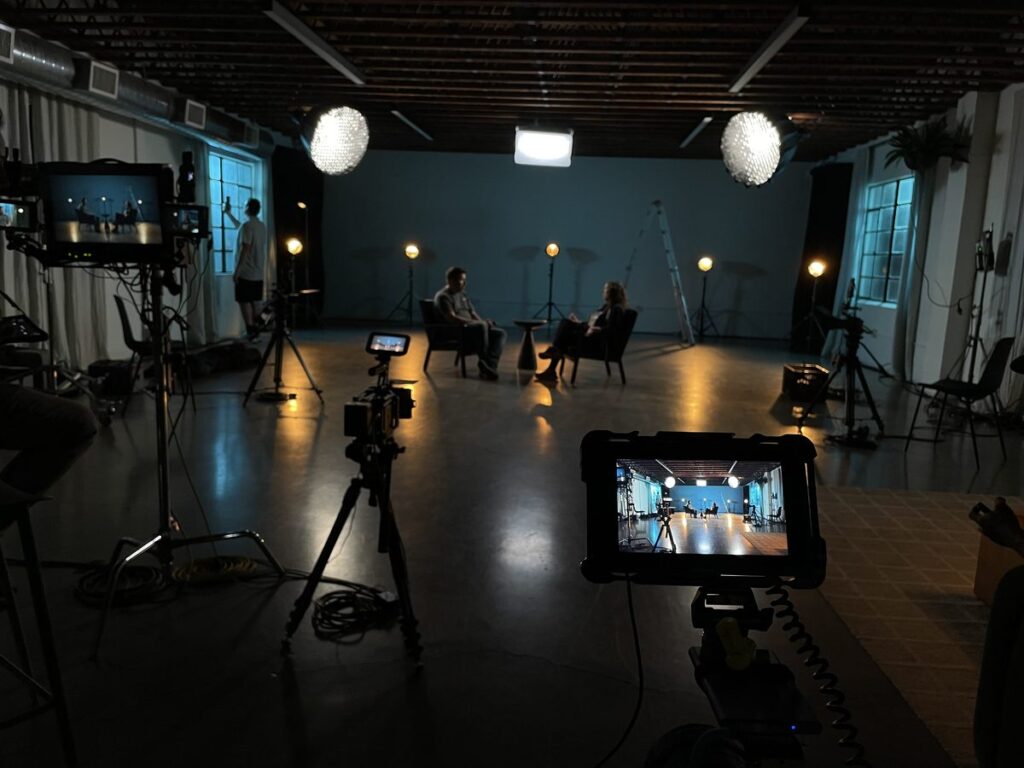 Tournage d'interview en studio professionnel par un vidéaste : éclairage scénique et plusieurs caméras sur trépied.