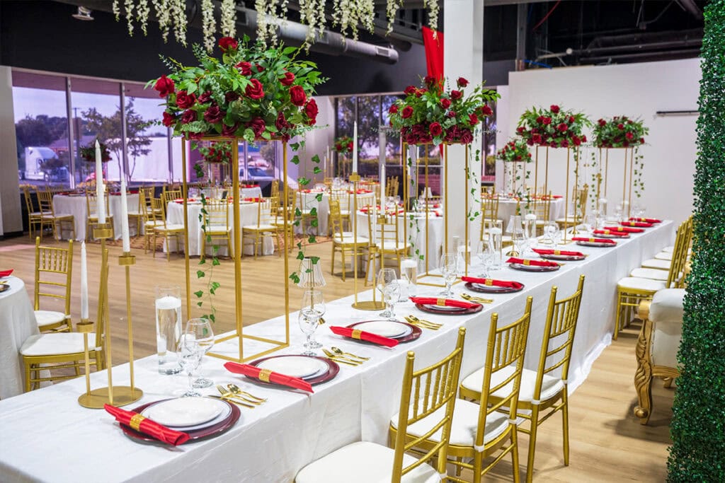 Indoor wedding planned in Nashville with long table and gold chairs, tall rose table accents, and dishware