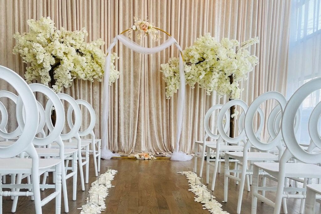 Indoor Tampa wedding aisle with white chairs, florals, and draped arch