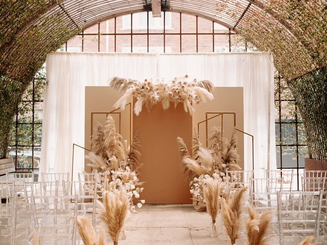 Interior wedding ceremony in Chicago with tan color scheme, archway, chairs, and plants