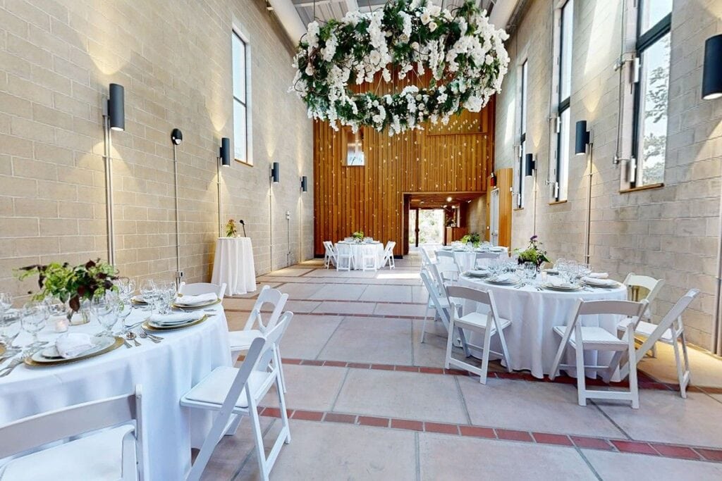Indoor Nashville wedding venue with wood panel wall, round tables with white chairs and centerpieces