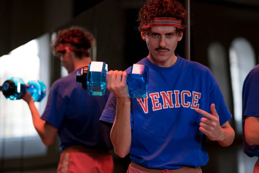 Man wearing a sweatband lifts a pretend weight as an homage to 80s weightlifting culture