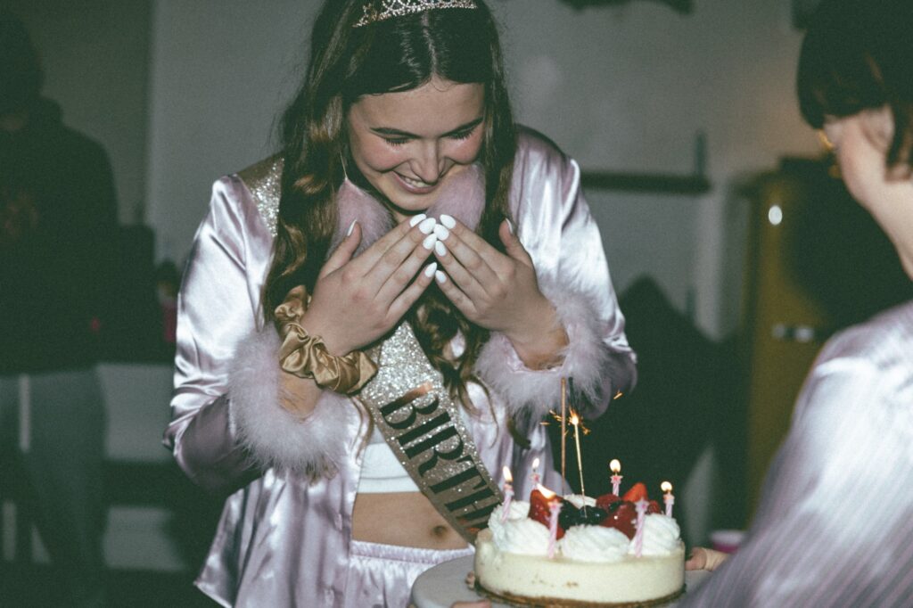 Birthday girl with sash looking at birthday cake at indoor party