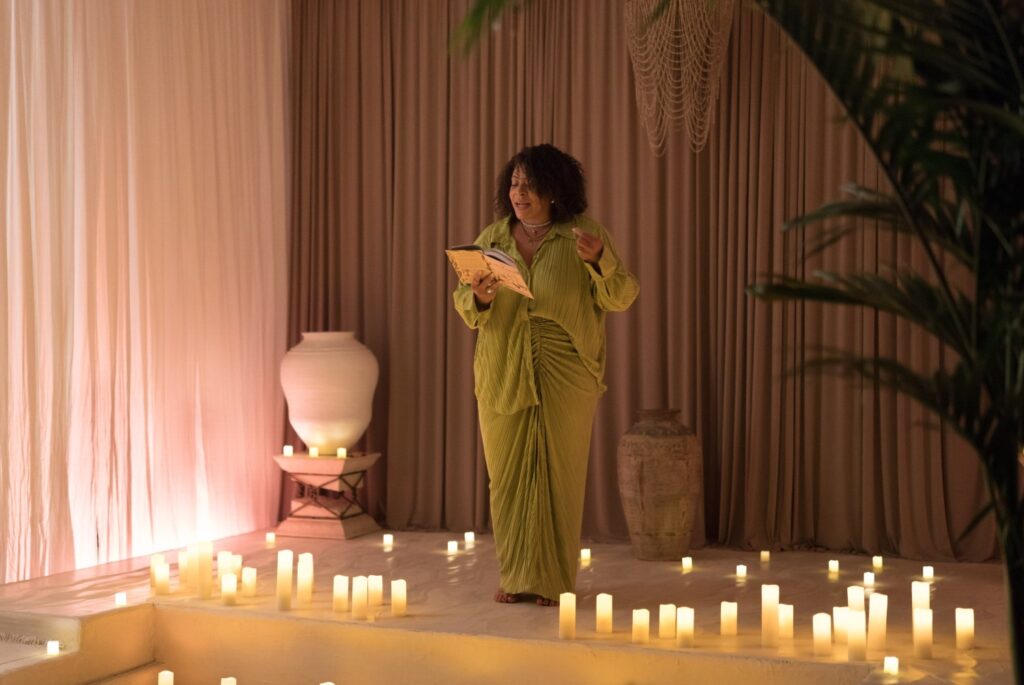 a woman speaking before a crowd surrounded by candles