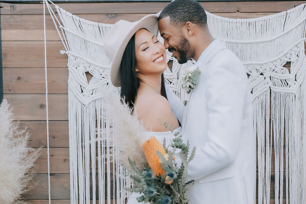 Boho chic California wedding couple posing against rustic macramé backdrop