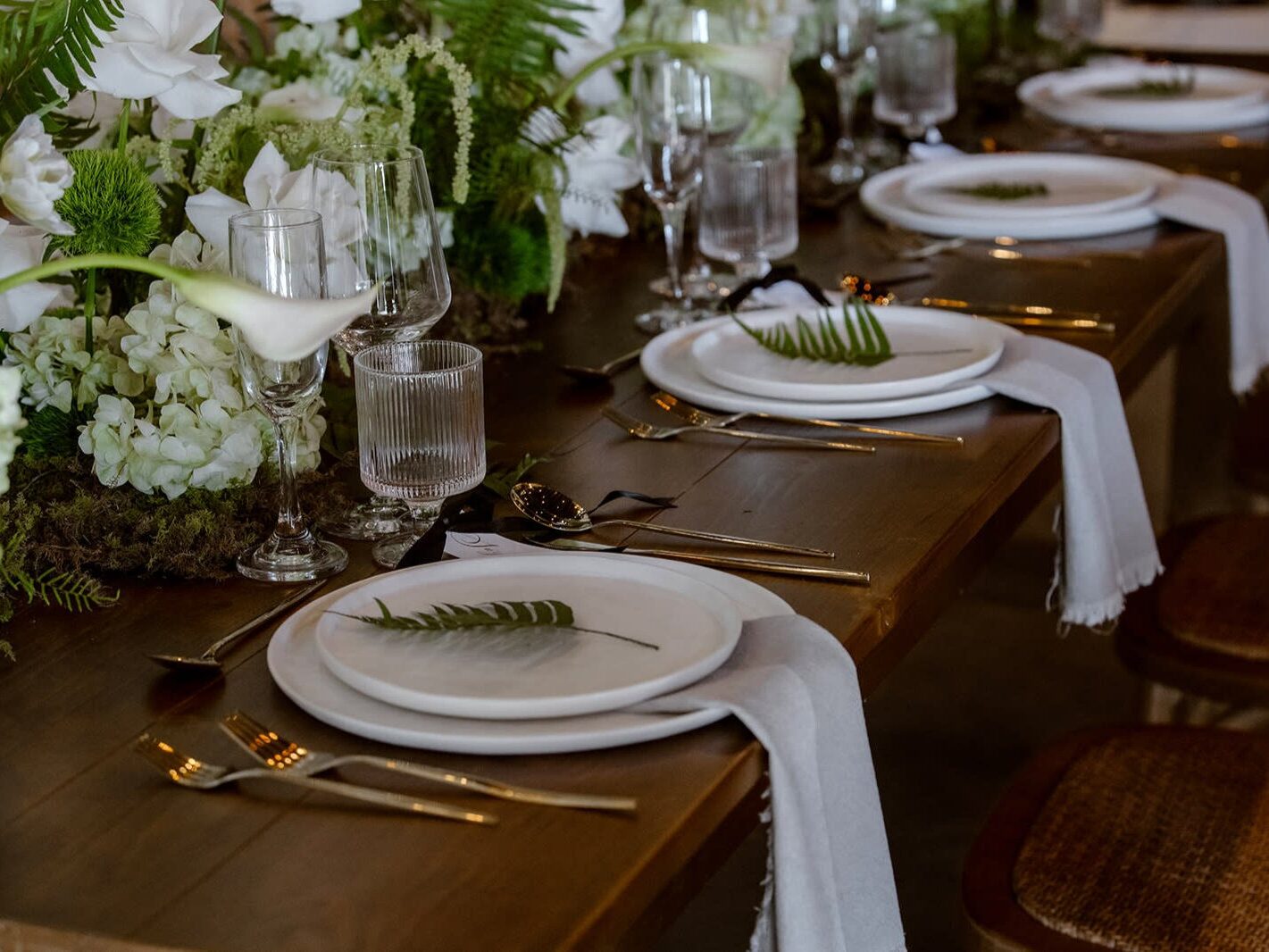 Place setting designed by wedding planner in Seattle featuring wine glasses, plates, and greenery