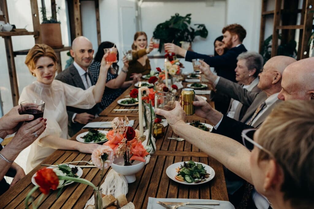 Friends and family toast at a small reception at a wooden table with brightly colored flowers