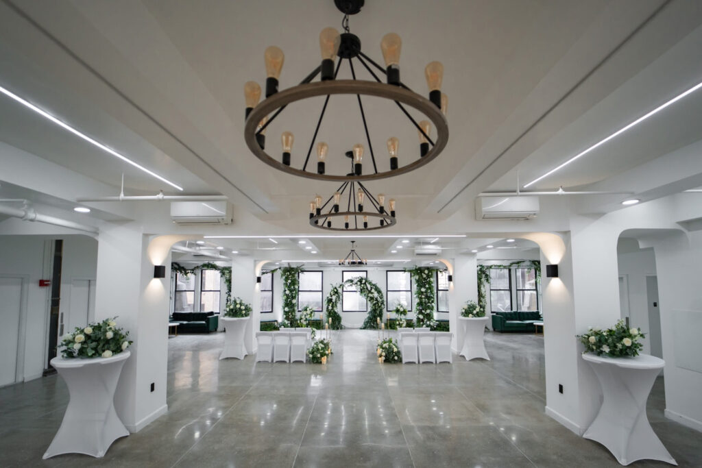 Bright, all-white New York City reception space punctuated by black windows, greenery and dark chandeliers