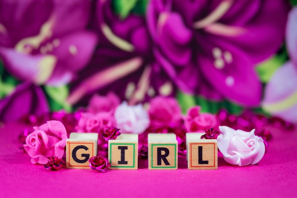 Little blocks spelling out "Girl" sit on a bright pink table surrounded by pink flowers at a baby event