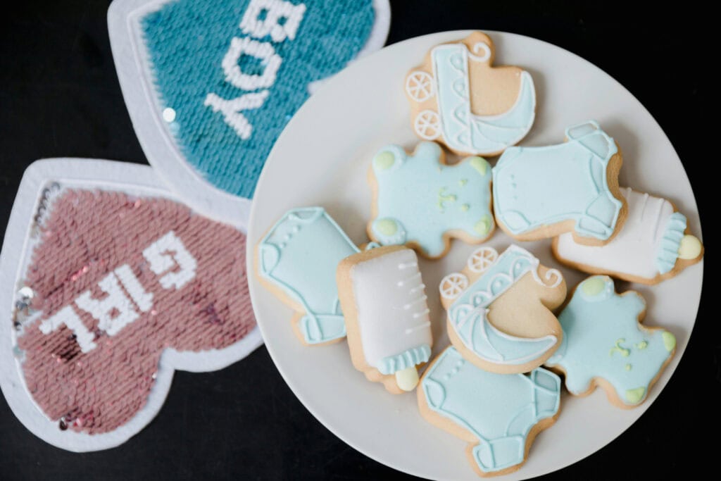 A plate of baby-themed cookies sit atop gender reveal boy/girl signs.