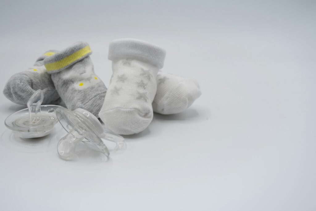 Gray and white baby socks sit next to two clear pacifiers