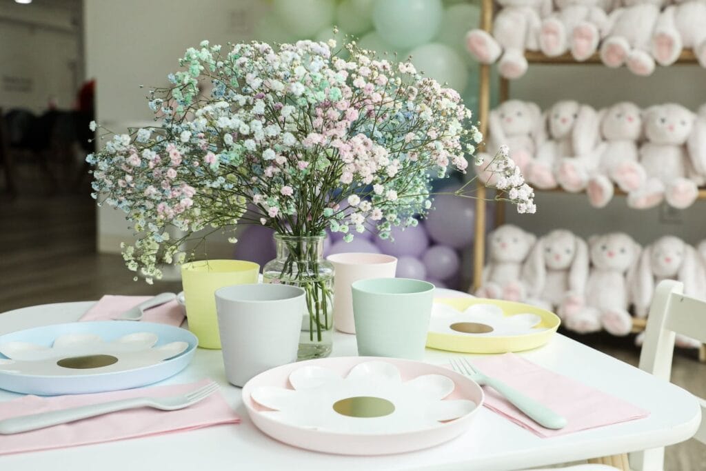 A vase of baby's breath on a table with pastel plates and shelves of stuffed bunnies in the background