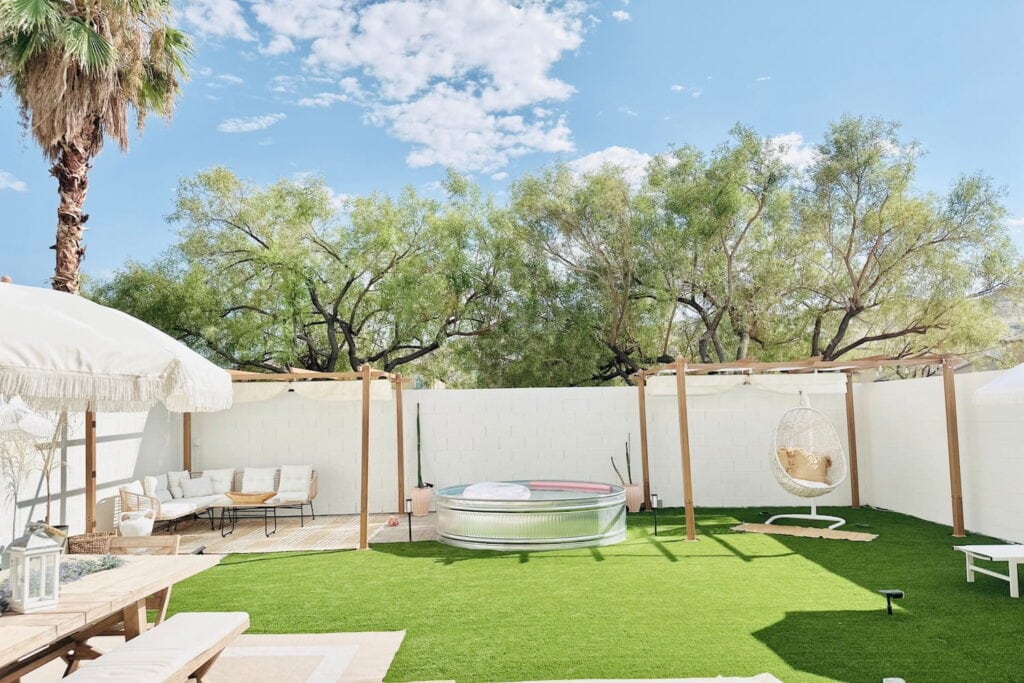 Bali-inspired backyard in Las Vegas with a stock tank pool, multiple seating areas and a picnic table with palm trees in the background