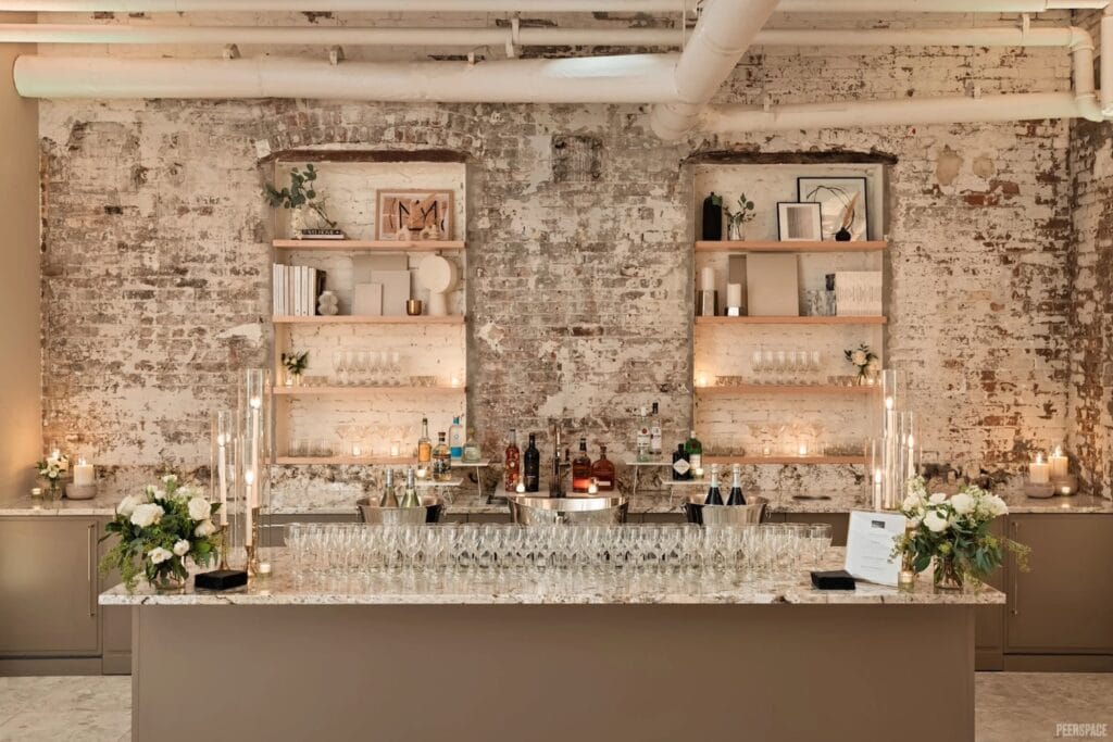 Wine glasses sit atop a bar in front of a white washed brick wall lit up by candles