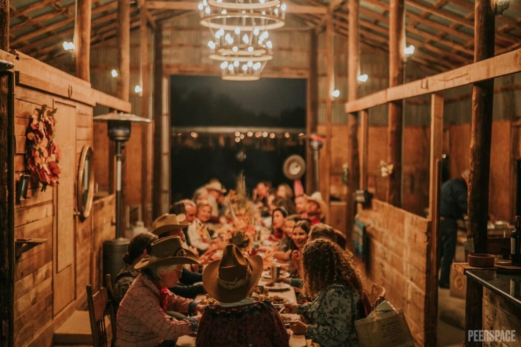 A large group gathers at a table set up in stables for a festive dinner