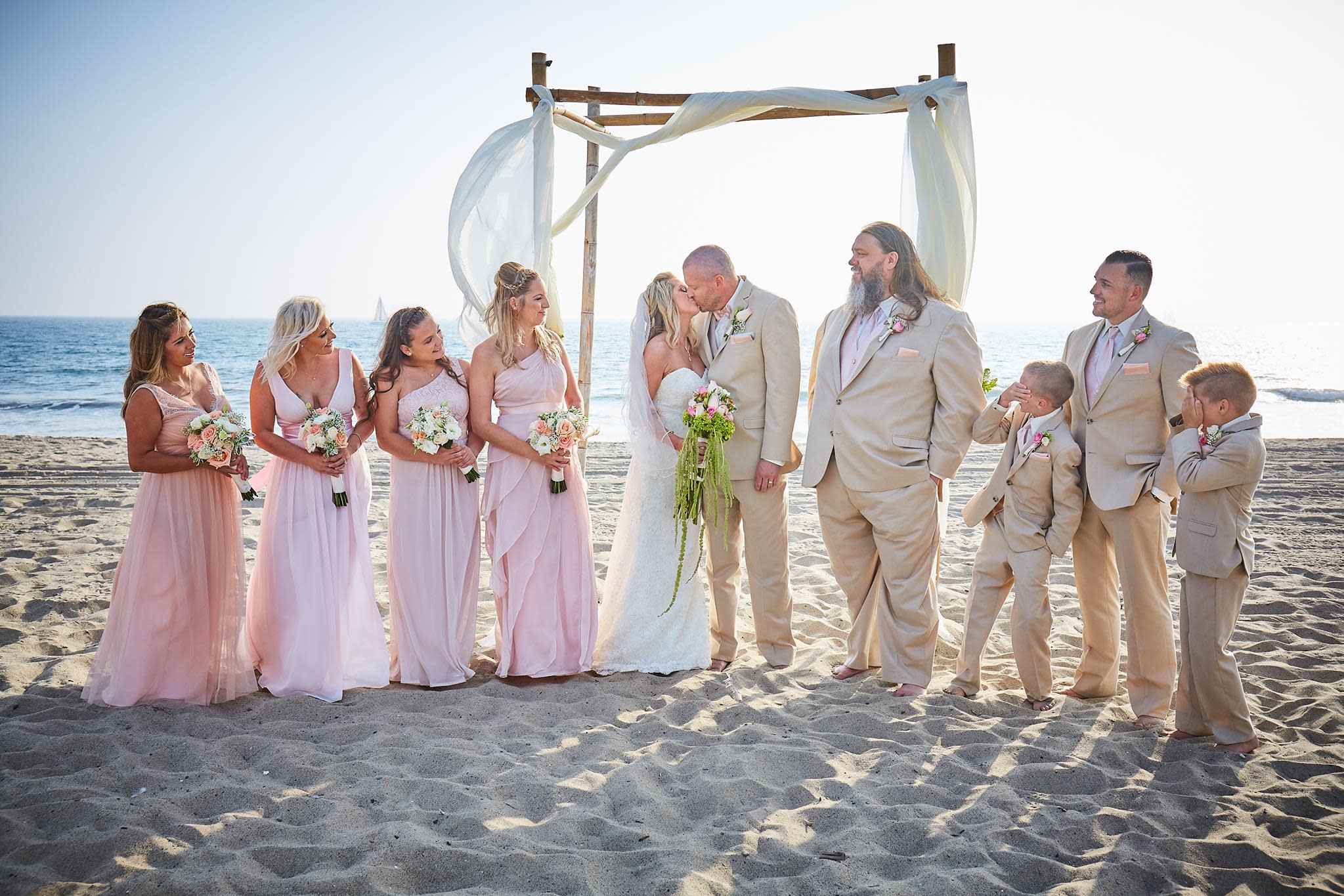 Bridal party under draped arbor at Long Beach beach wedding ceremony