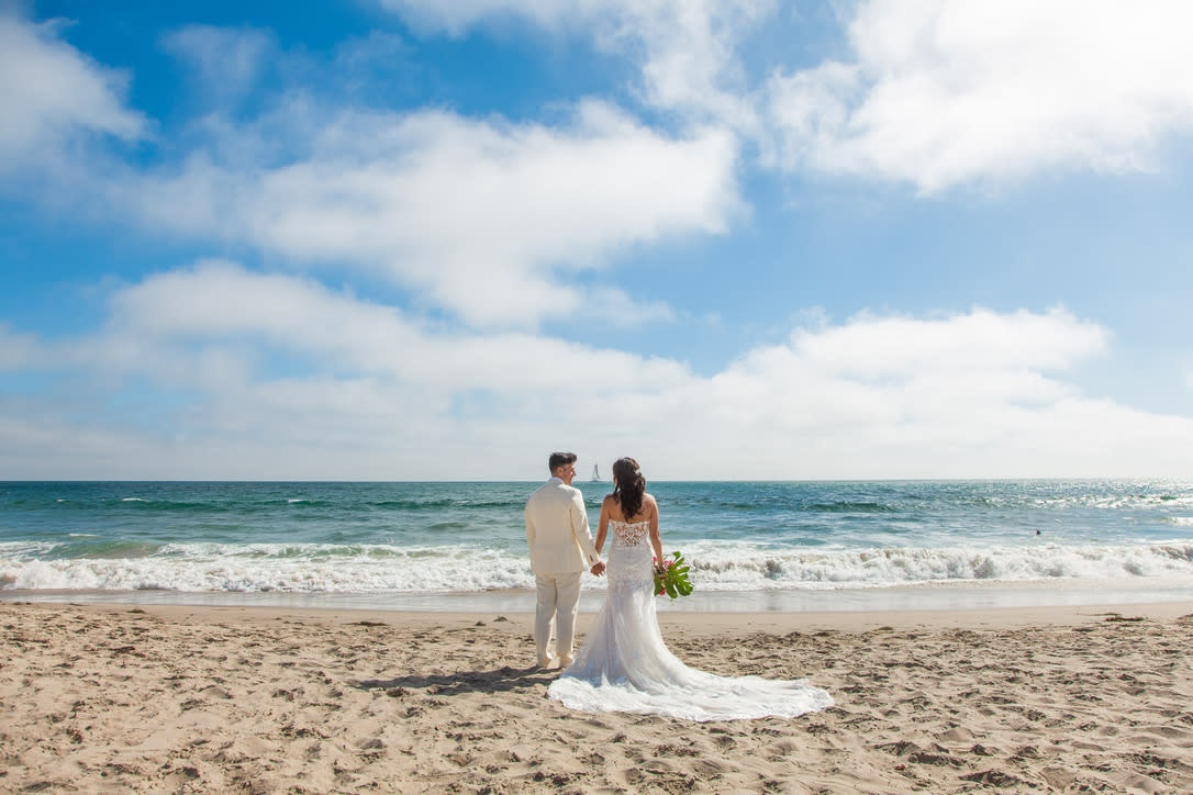 Bride and groom holding hands facing ocean waves on Long Beach shore