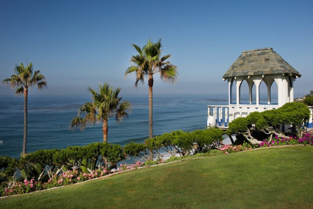 A beachfront gazebo with lush surroundings including palm trees and pink and purple flowers