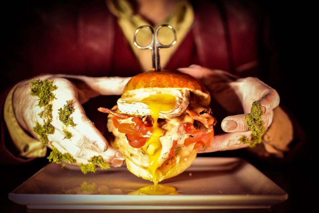 Closeup of hands holding a loaded sandwich dripping with yellow sauce
