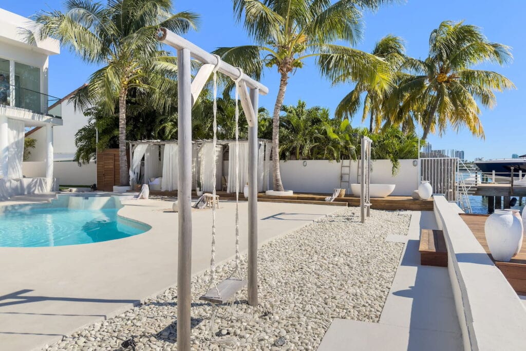 Bali-inspired backyard in Biscayne Bay, Florida with white concrete and rocks, wooden swings and cabanas